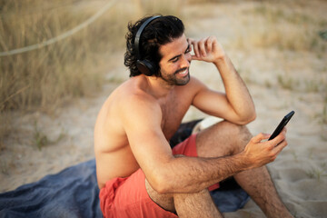 Young man sitting on the beach. Young man listening the music while relaxing at the beach