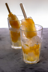 Two glass glasses are on the table. They contain ice, pieces of orange fruit and homemade ice cream