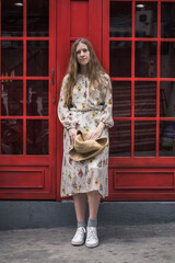 Obraz premium Beautiful caucasian young woman in dress and sneakers standing on the street in London and smiling. Long straight blond hair. Red english phone booth