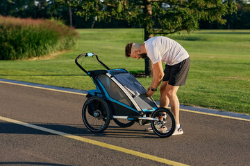 Young father is walking with his son in a baby carriage at city park. Dad with child pram outdoor workout