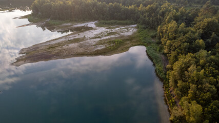 Aerial view shot by a drone of the shore of a forest lake. Thick grass, reflections in the water, green birches in the distance on the slope. Nature of the Blakheide, Beerse, Belgium. High quality