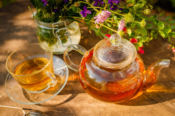 Summer healthy herbal tea in glass teapot and bunches of medicinal herbs on wooden board Phytotherapy. Herbal medicine. Bouquet of wildflowers and medicinal herbs for herbalists