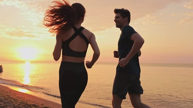 Back view young couple two friends family man woman together wear sports clothes warm up warm up train running jogging at sunrise sun dawn over sea beach outdoor on pier seaside in summer day evening