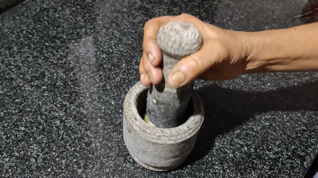 Put a vegetable food item inside a pestle and mortar on a granite surface in the kitchen and crush it for the purpose of making dish