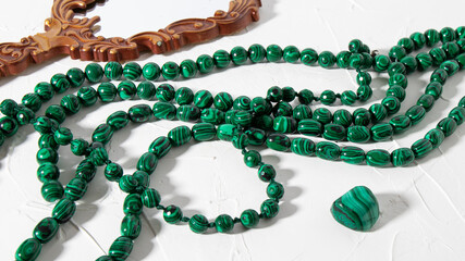 Beautiful green beads made of Russian malachite on a white plastered background. Natural energetic...