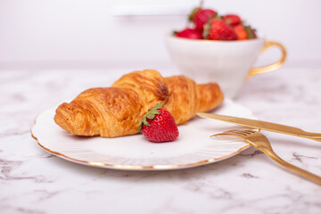Cup with fresh strawberry and tasty croissant on white plate