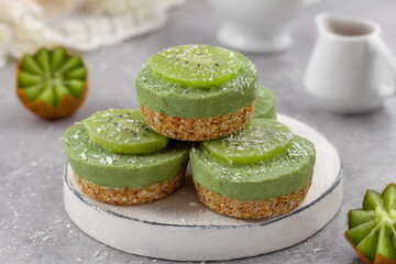 Mini avocado cheesecakes on a nut, coconut and date crust topped with kiwi slices. Raw vegan dairy...