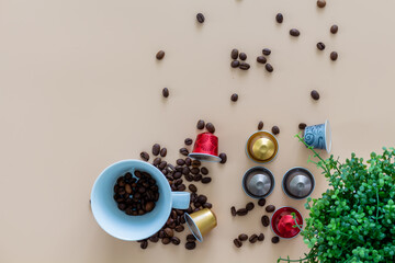 Coffeebreak with a cup of coffee, capsule, coffeebeans and green plant on beige background