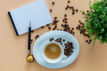 Obraz na płótnie Canvas A blank paperblock for a concept Coffeebreak with a cup of coffee, coffeebeans with green plant on beige background. Concept for sustainable concept