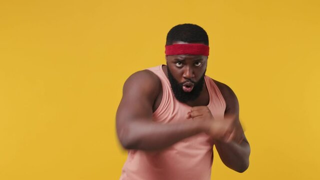 Fitness trainer instructor sporty young bearded african american man sportsman 20s in headband pink tank top warm up making boxing exercises in home gym isolated on plain yellow background studio