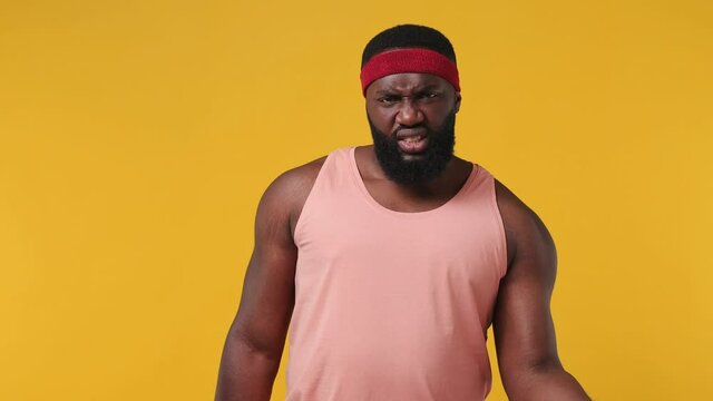 Serious concentrated trainer instructor sporty young bearded african american man sportsman 20s in headband pink tank top lifting small dumbbell in home gym isolated on plain yellow background studio