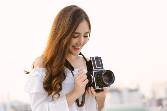 Beautiful young Asian stylish woman taking photos with retro film camera on the rooftop of a building. Asian girl smiling enjoy weekends, Holiday lifestyle trip.