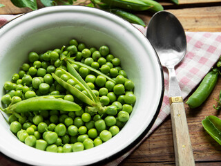 Fresh green peas in a white bowl, pods, on the table 