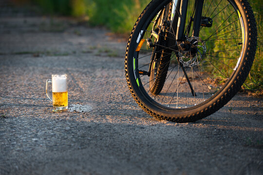 In the open air there is a bicycle close-up, next to a glass filled with beer.