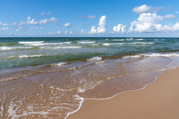 idyllic sandy beach with gentle waves lapping at the shore under a blue summer sky with white...