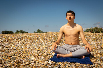 Naklejka na ściany i meble Teenage boy on a beach meditating