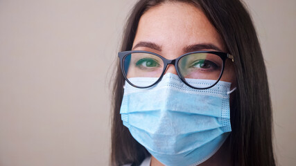 Close up of young brunette woman doctor with glasses and light blue protective mask copyspace