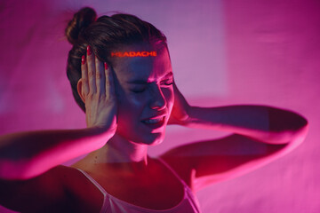 Young adult woman holds hands on head ad having suffering facial expressions with word Headache on her face.