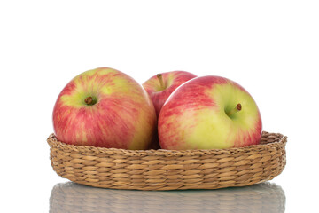 Three juicy organic apples in a bowl made of straw, close-up, isolated on white.
