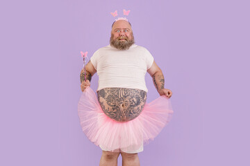Excited obese mature man with large bare abdomen wearing fairy suit holds magic stick and chiffon...