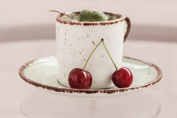 A cup on a green saucer  and wwo red cherries. Still life with cherries