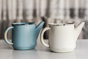 Obraz premium Two rustic watering pots, white and blue on white wooden table . Vintage rustic kitchen style