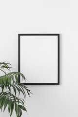 Black frame mockup on the wall with a palm plant.