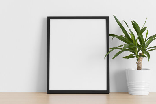 Black frame mockup with a yucca plant on the wooden table.