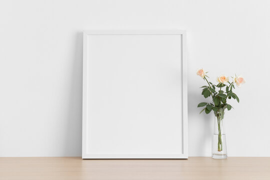 White frame mockup with a bouquet of a pink roses on the wooden table.