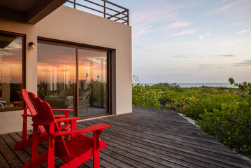 wooden deck terrace with two red chairs overlooking the beach, vegetation and ocean with the...
