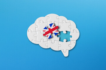 English learning concept, white jigsaw puzzle pieces with british flag a human brain shape on blue...