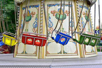 The picture shows a carousel in a calm state with multi-colored seats hanging from chains in the...