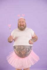 Funny emotional plus size man with bare tummy wearing fairy costume holds magic stick posing on...