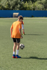 The boy loves to play football, trains with the ball on the artificial turf and scores a goal.