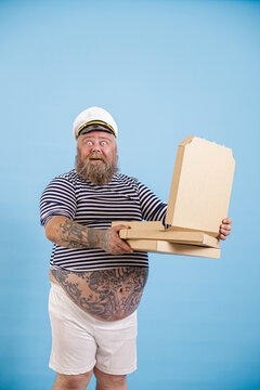 Happy Surprised Middle Aged Man With Overweight In Sailor Suit Holds Open Box Of Delicious Pizza Standing On Light Blue Background In Studio