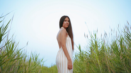 young woman in striped dress with straps and halter neckline posing in the field