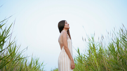 young woman in striped dress with straps and halter neckline posing in the field