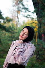 Muslim woman in hijab on the background of trees. Pink blouse and black skirt. Beautiful young woman. Close-up.