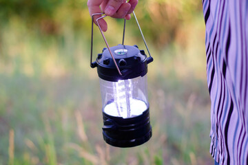 A woman holds a lamp by the handles in her hands. Compass on the lamp. Camping LED lamp.