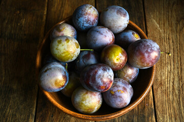 Home harvest fresh plums in earthenware on a wooden table. View from above.