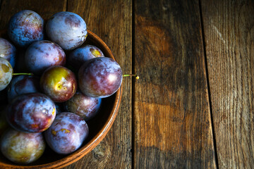 Home harvest fresh plums in earthenware on a wooden table. View from above.