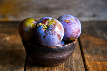 Home harvest fresh plums in a ceramic bowl on a wooden table.