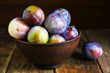 Home harvest fresh plums in a ceramic bowl on a wooden table.