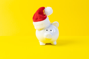 Creative composition with piggy bank in Santa’s hat on bright yellow background. Christmas bank promotions and deposits concept. Festive New Year and Christmas shopping.