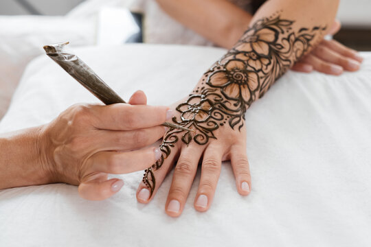 Mehndi artist drawing floral henna tattoo on woman hand in beauty salon. Master applying traditional mehendi pattern for bride before wedding.