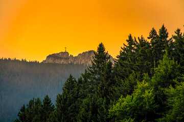 View at the hiking destination at the Kampenwand cross at a wonderful golden hour light from far away at the peak of the alpine mountain peak.