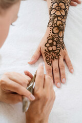 Mehndi artist drawing floral henna tattoo on woman hand in beauty salon. Master applying traditional mehendi pattern for bride before wedding.