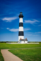 A vertical landscape of the Bodie Island Lighthouse front view under a cloudy blue sky.