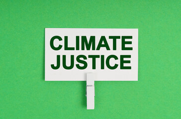 On a green background, a business card on a clothespin. The business card says - Climate justice