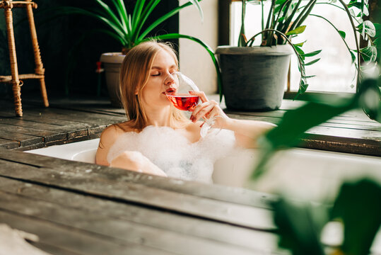Beautiful young woman drinking champagne and looking to the camera enjoying bubble bath